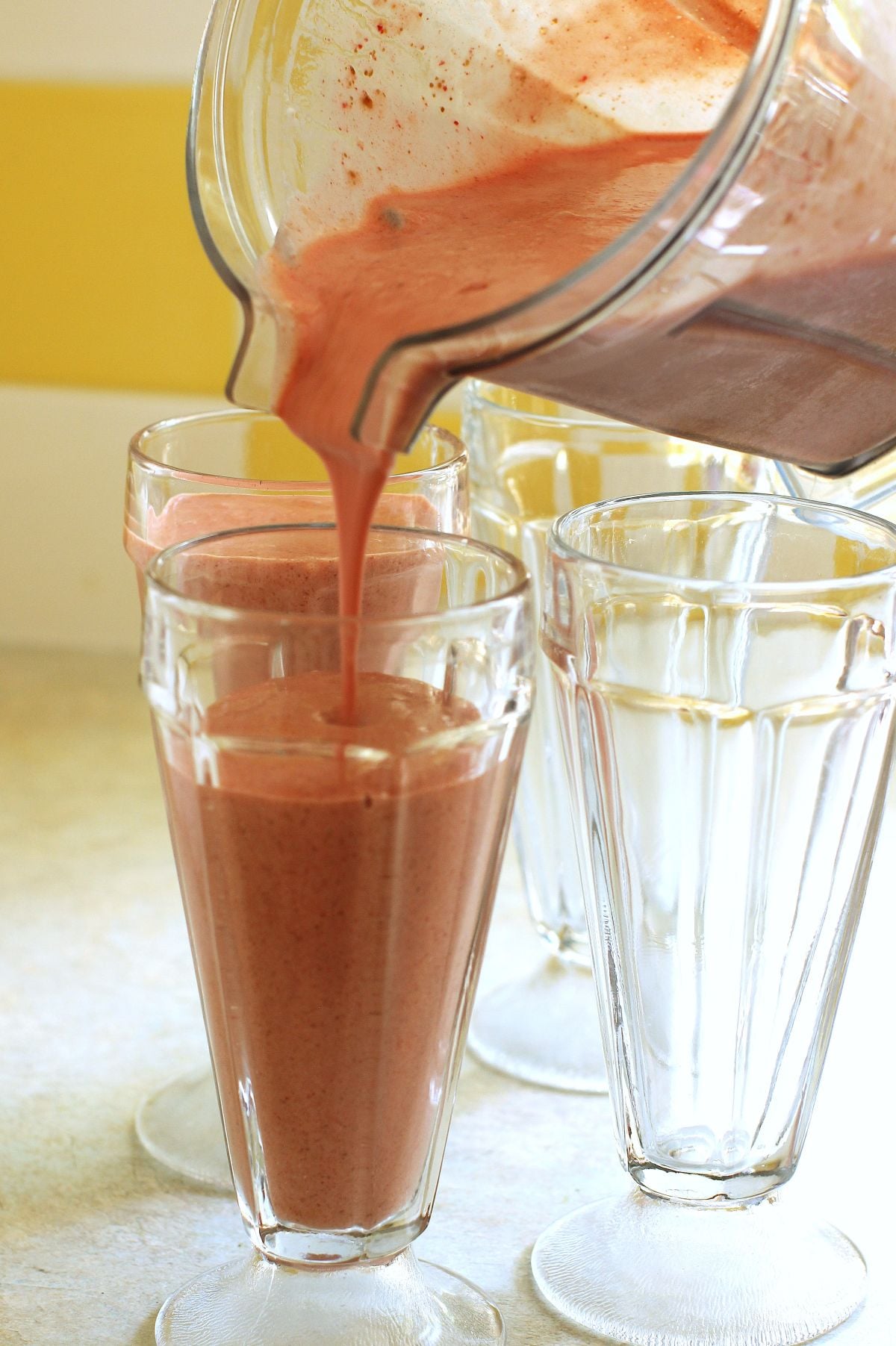 Pouring smoothie from the blender into tall glasses.