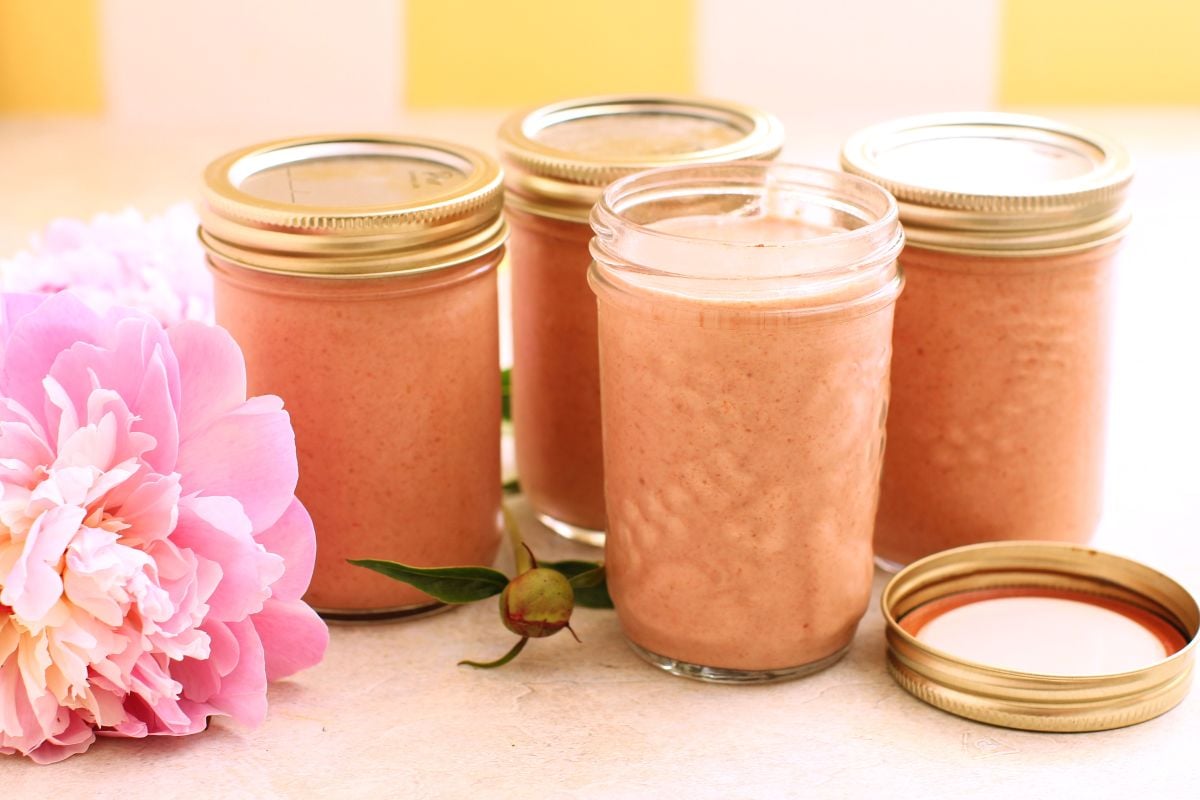 4 small half-pint jars of smoothie, with a peonie laying beside them.