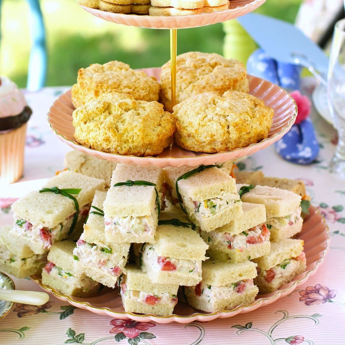 Square thumbnail photo with the bottom of a 3-tiered cake stand holding Strawberry Chicken Salad Sandwiches and the middle holding scones.