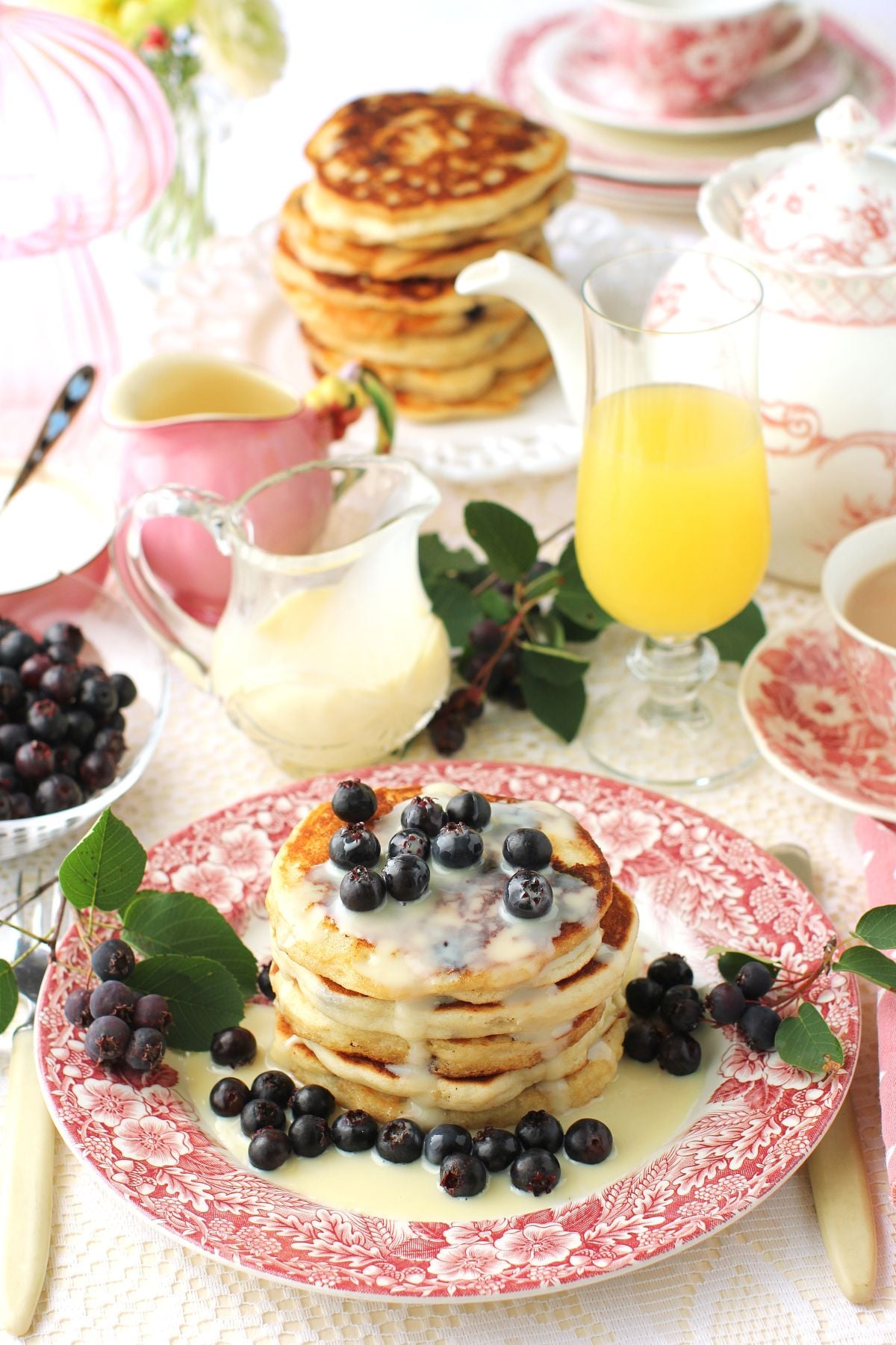 Breakfast table set with pink and white transferware dishes and a plate of saskatoon pancakes drizzled in sweetened condensed milk with lots of fresh saskatoons.