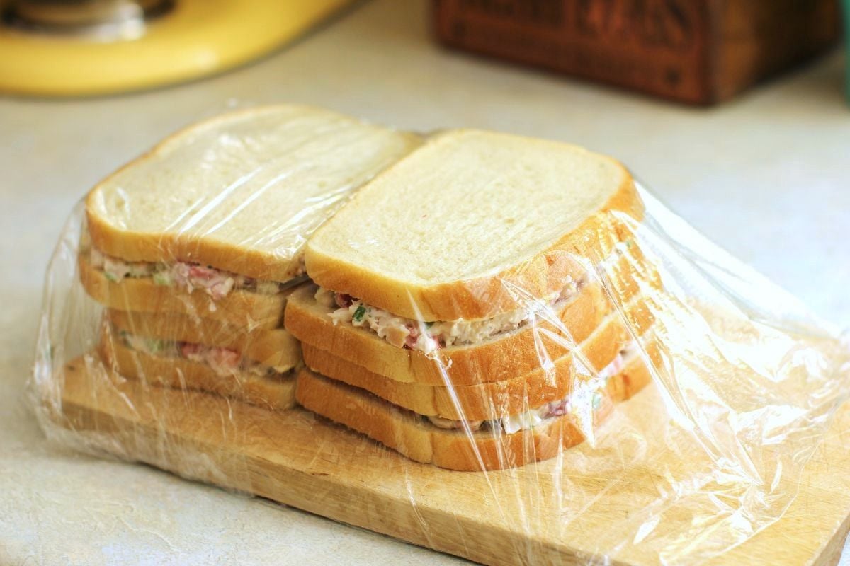 Stacks of sandwiches on a cutting board, wrapped with clingwrap.