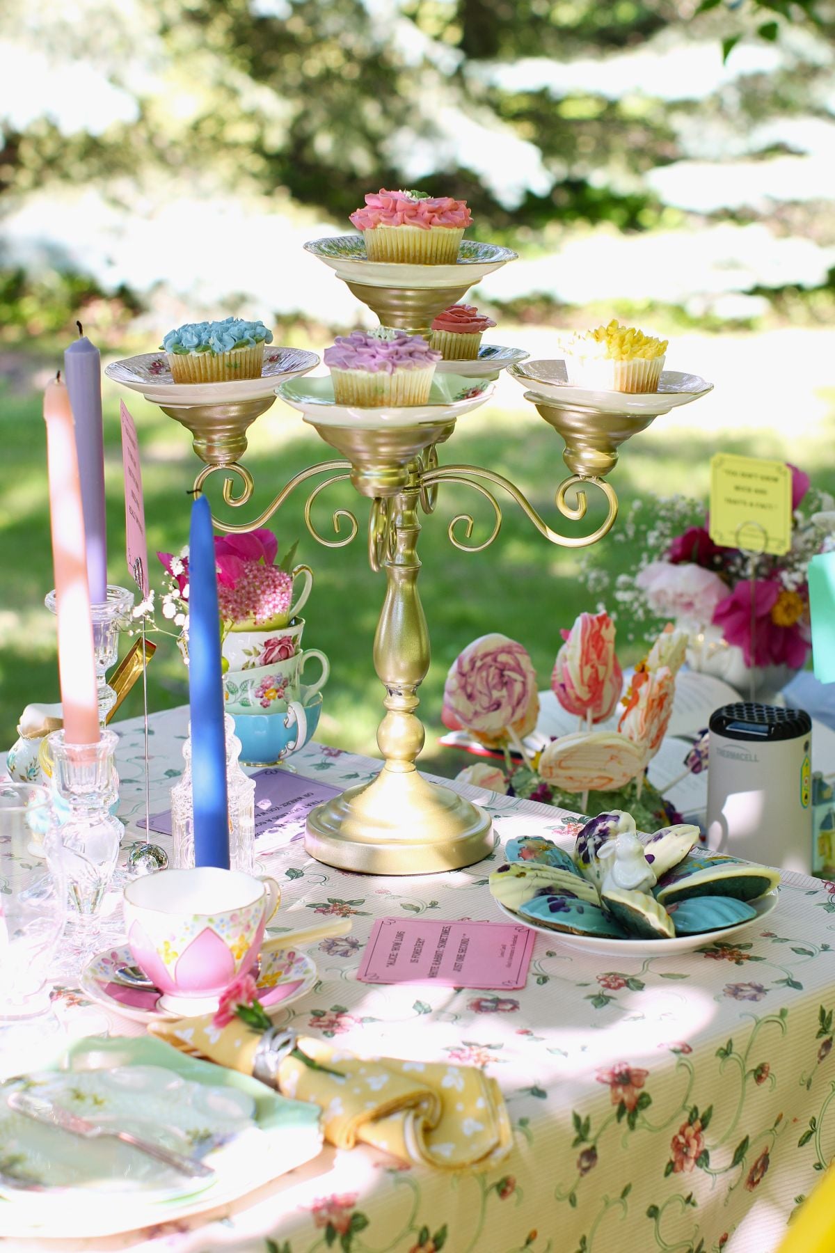 Candelabra stand on tea table with cupcakes on each saucer of the stand, plus crystal candleholders with pastel candles in them.