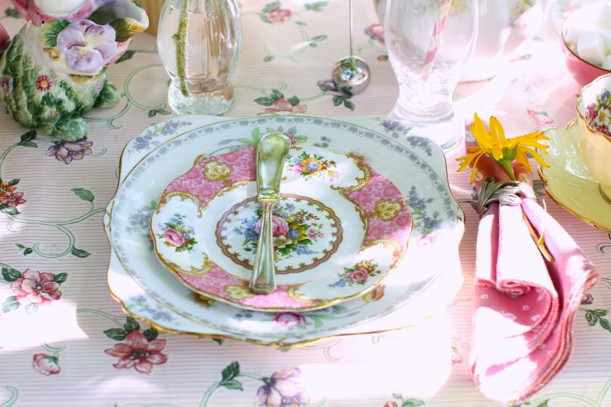 Table setting with mismatched china plates and a butter spreader on a pink flowered tablecloth.