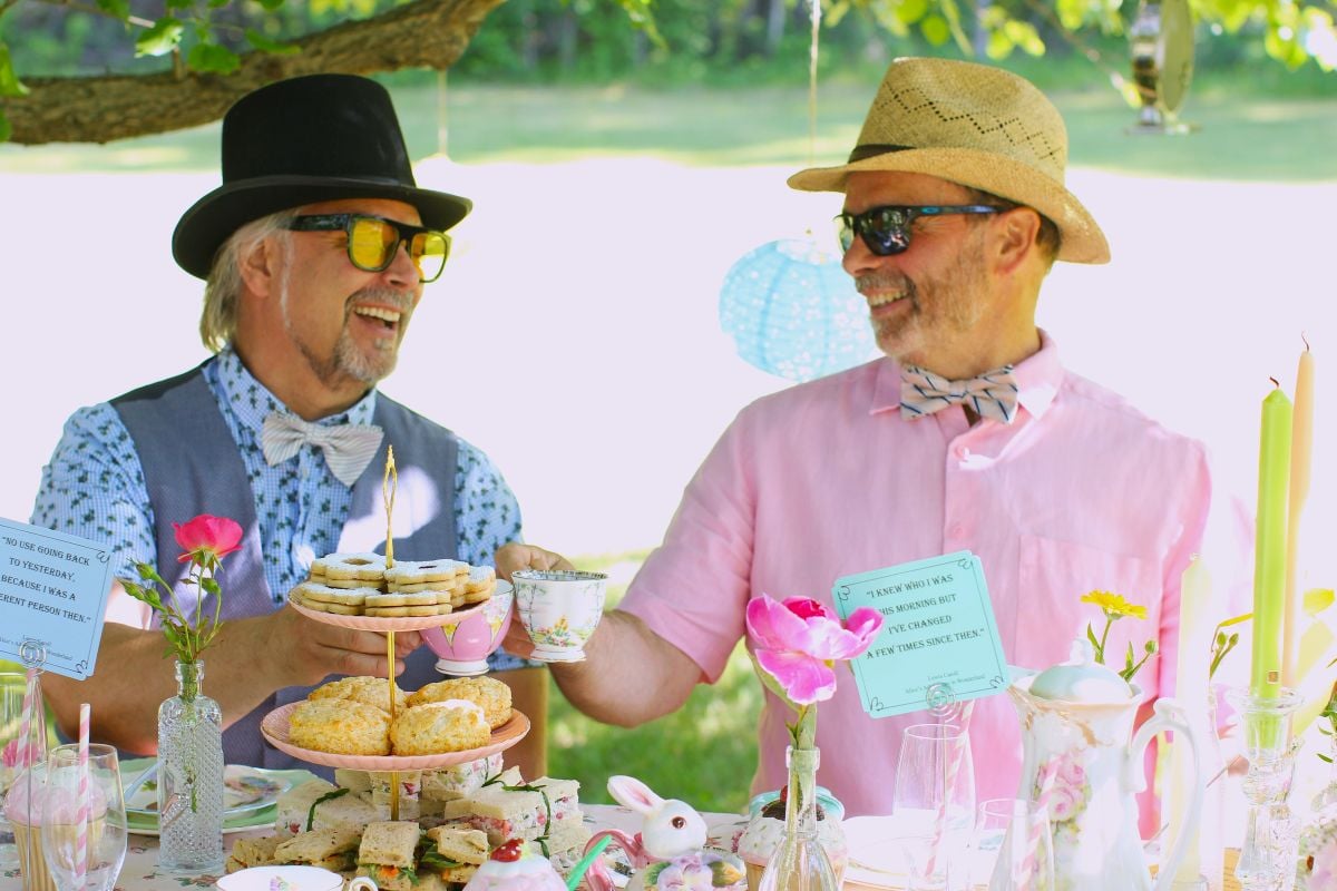 Loreto and Raymond wearing hats, toasting with their tea cups.