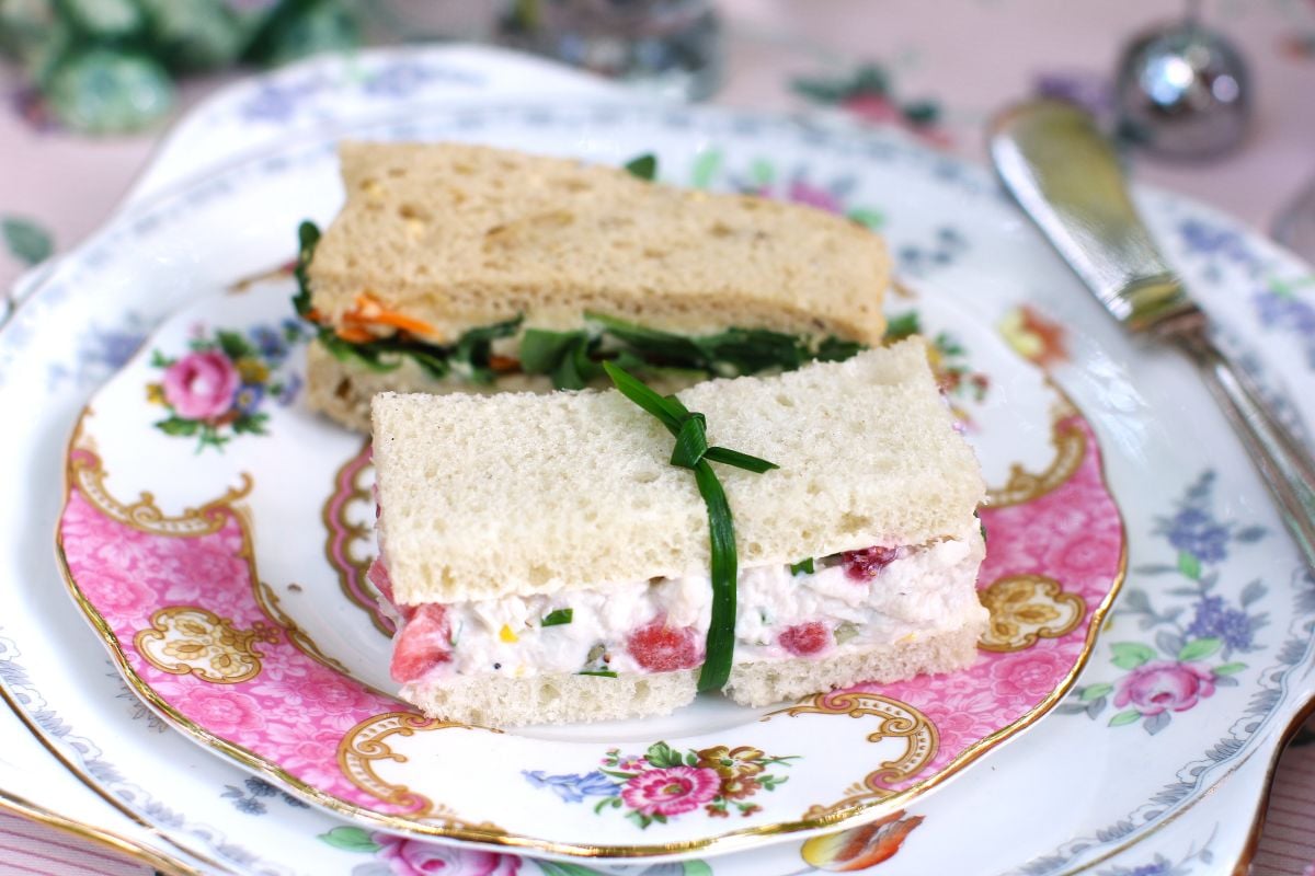 Two finger sandwiches on a pink flowered china plate, the strawberry chicken salad sandwich on white bread in front.