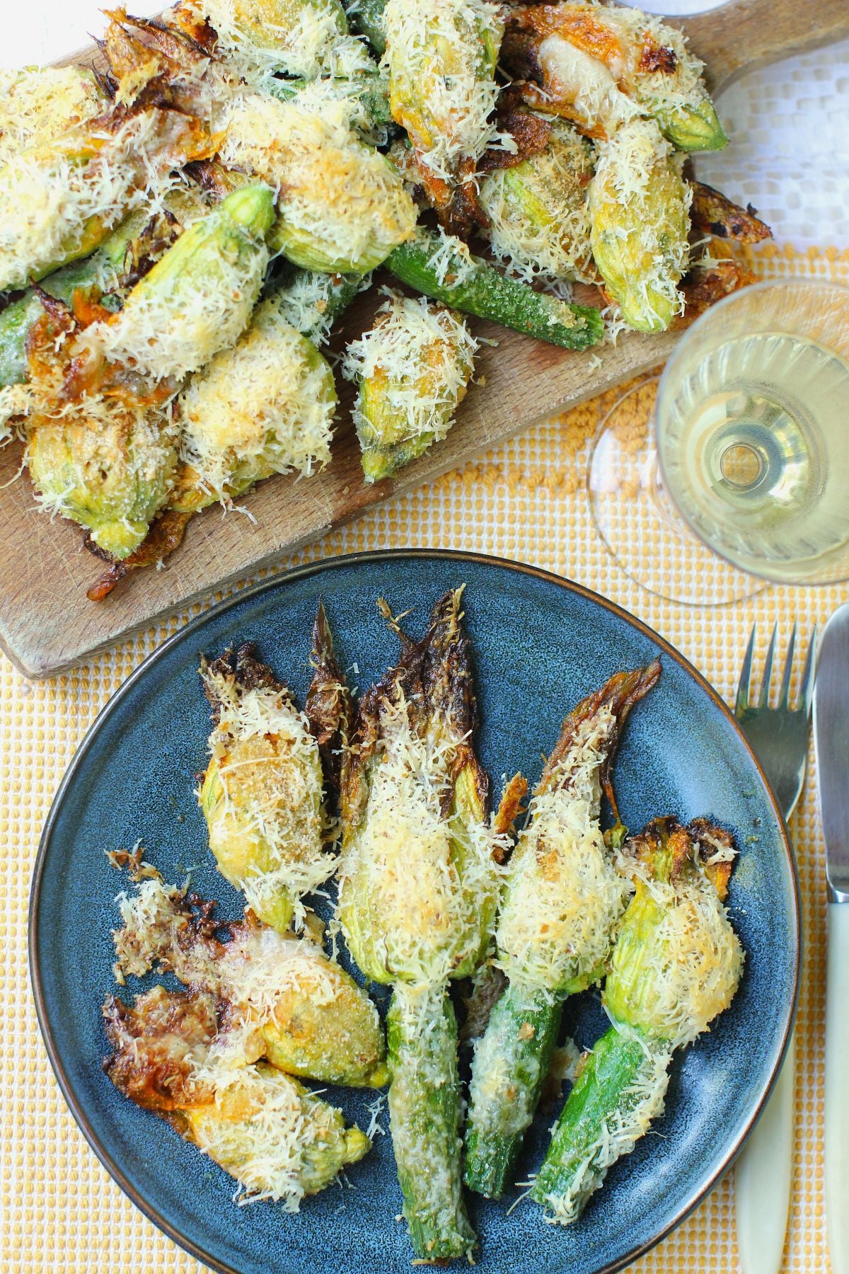 Blue Plate with baked stuffed zucchini blossoms fanned out on it, a glass of wine, and more stuffed zucchini blossoms on a cutting board in top left corner.