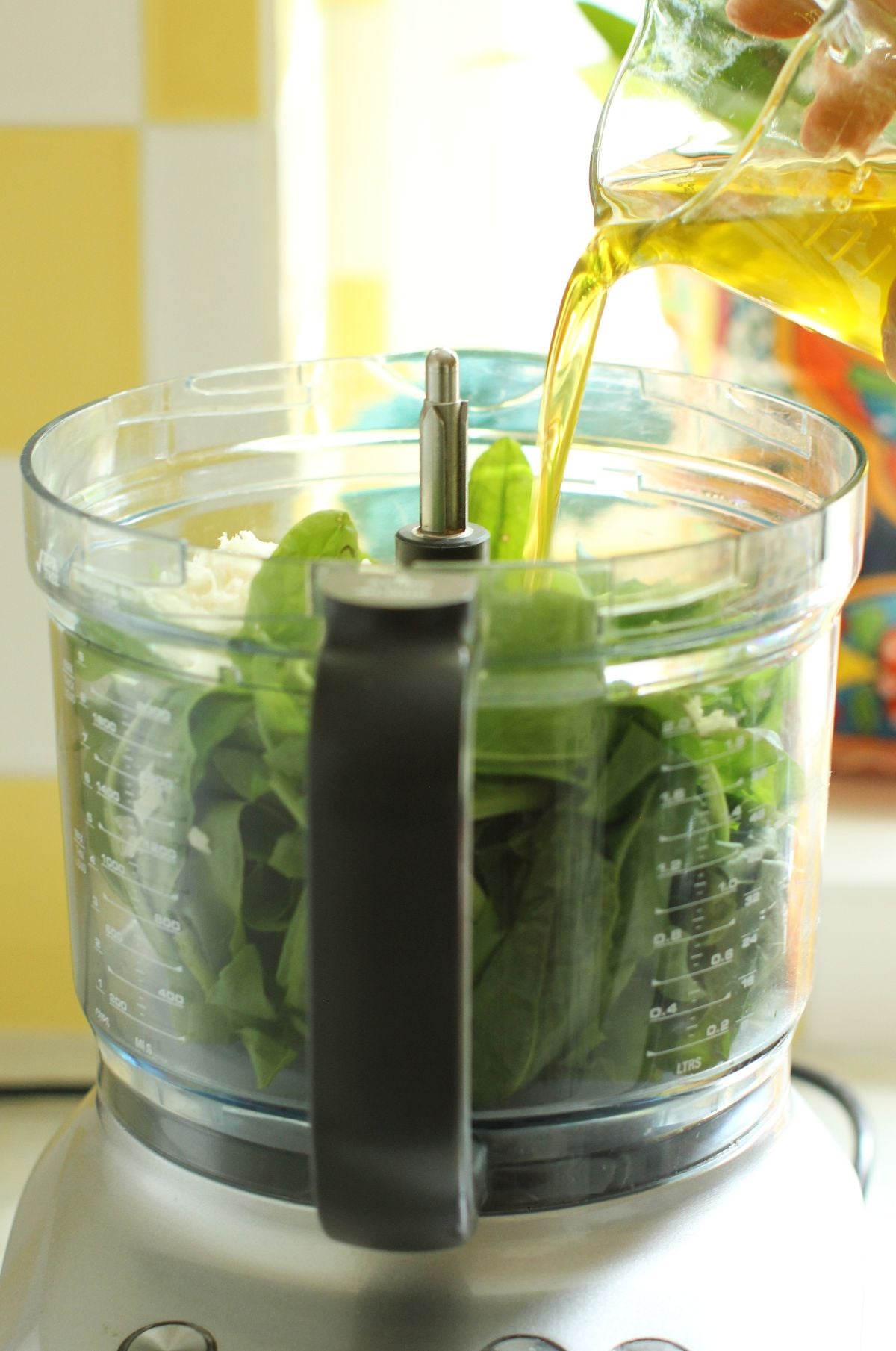Stream of oil being poured into the food processor canister whichis filled with sorrel leaves.