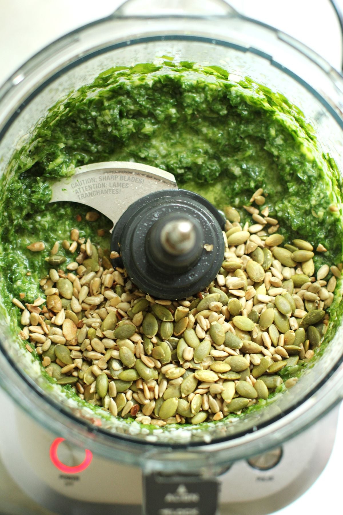 Looking down into food processor canister to the green paste and whole sunflower and pumpkin seeds.