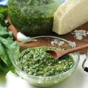 Square thumbnail image of a clear glass bowl of sorrel pesto with a jar of it behind, and a chunk of Parmesan cheese.