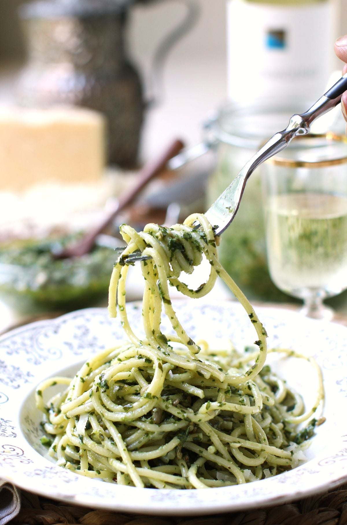 a fork lifting strands of spaghetti coated with sorrel pesto in a rimmed white soup plate.