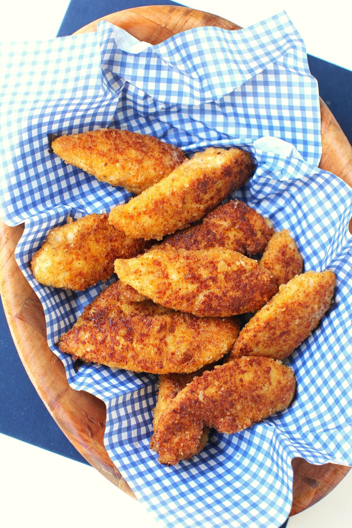 Cheesy chicken fingers in an oval wooden bowl lined with white and blue checked paper.