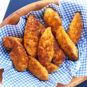 Square thumbnail photo of a pile of cheesy chicken fingers on blue & white checked paper in a wooden bowl.