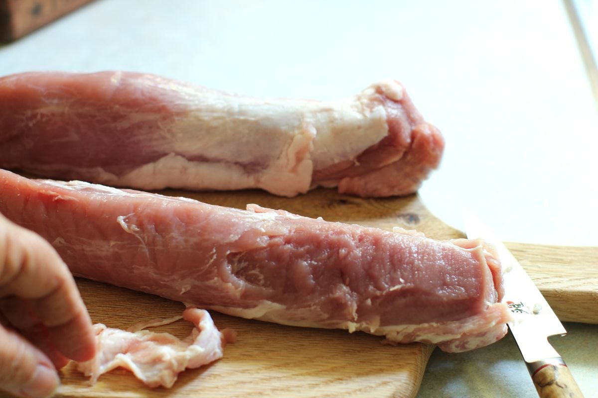 Two raw pork tenderloins on a cutting board, the front one with the silverskin removed.