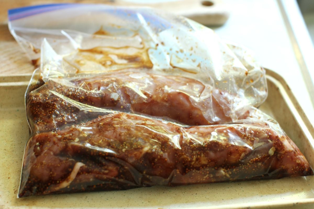 Plastic bag of marinating pork tenderloins in a pan.