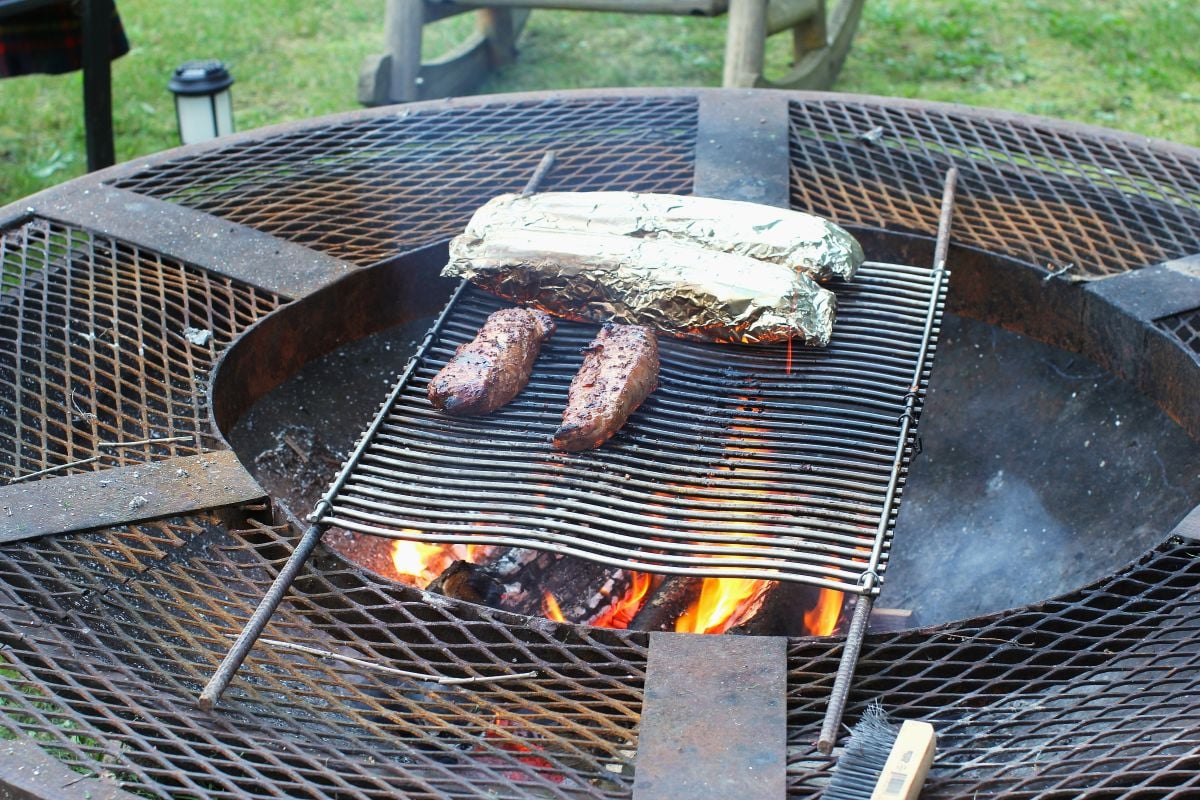 Two grilled tenderloins and two foil packs of potatoes on the grill on the fire pit.