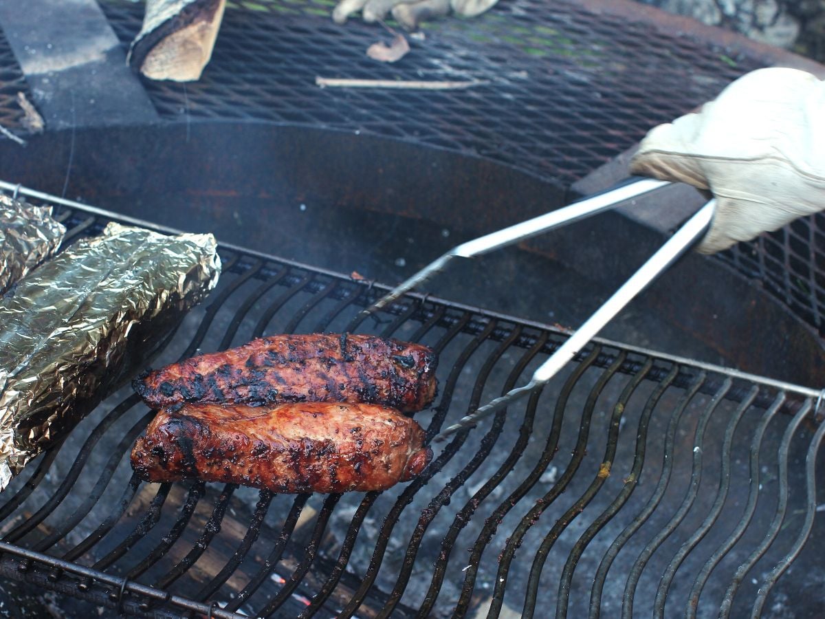 Turning the grilled tenderloins with tongs and leather gloves.
