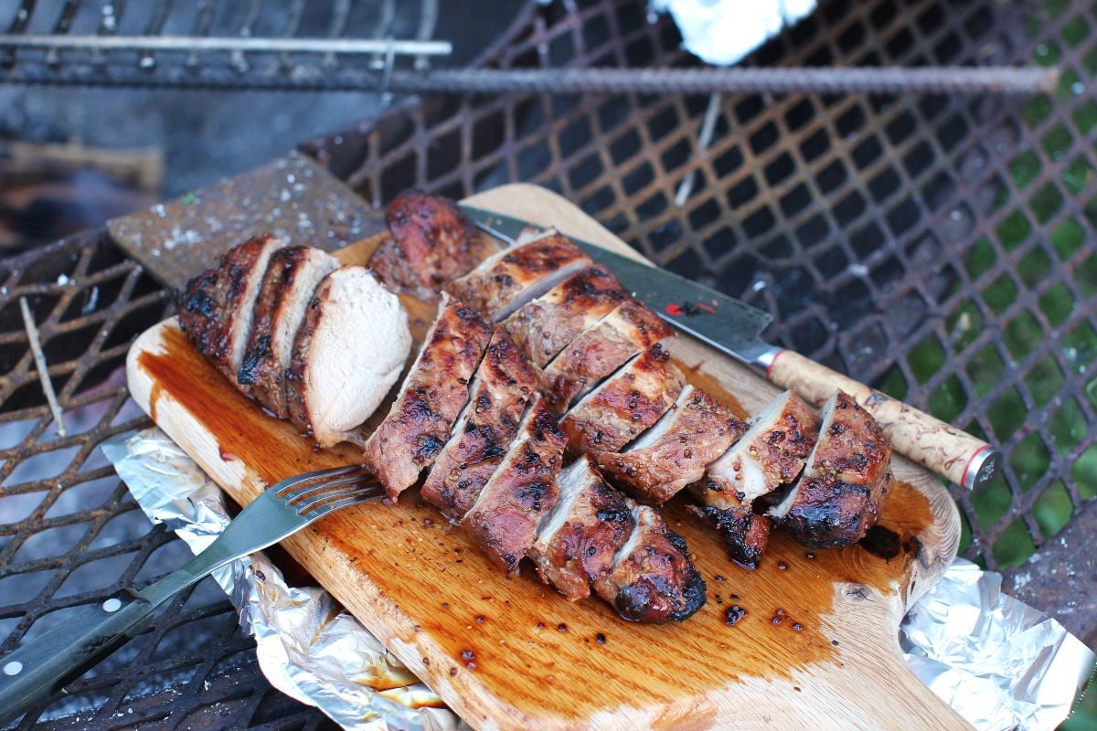Sliced grilled tenderloin on a cutting board with foil underneath, on the fire pit.