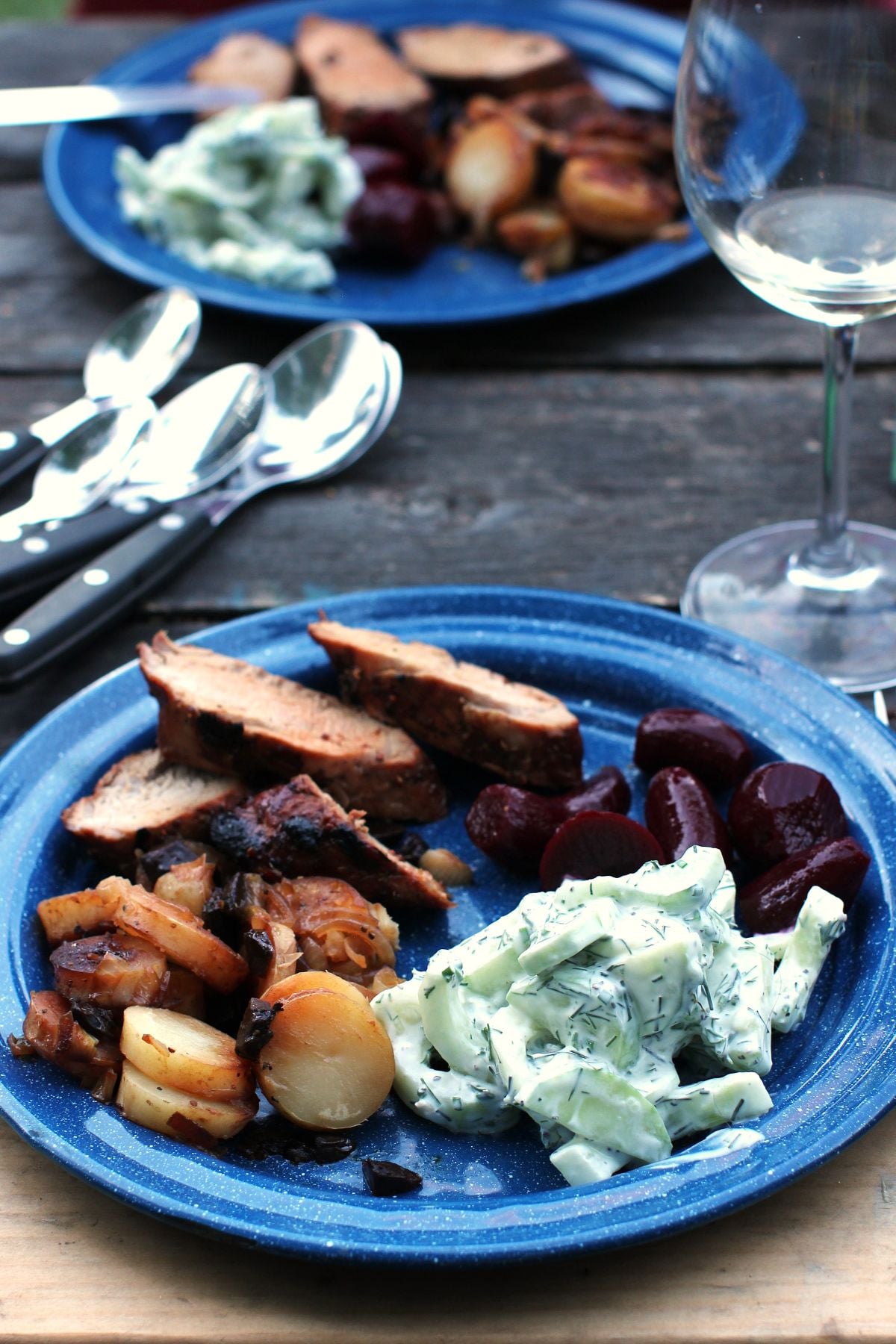 Blue enamelware plate filled with sliced grilled tenderloin, campfire potatoes, cucumber salad, and pickled beets.